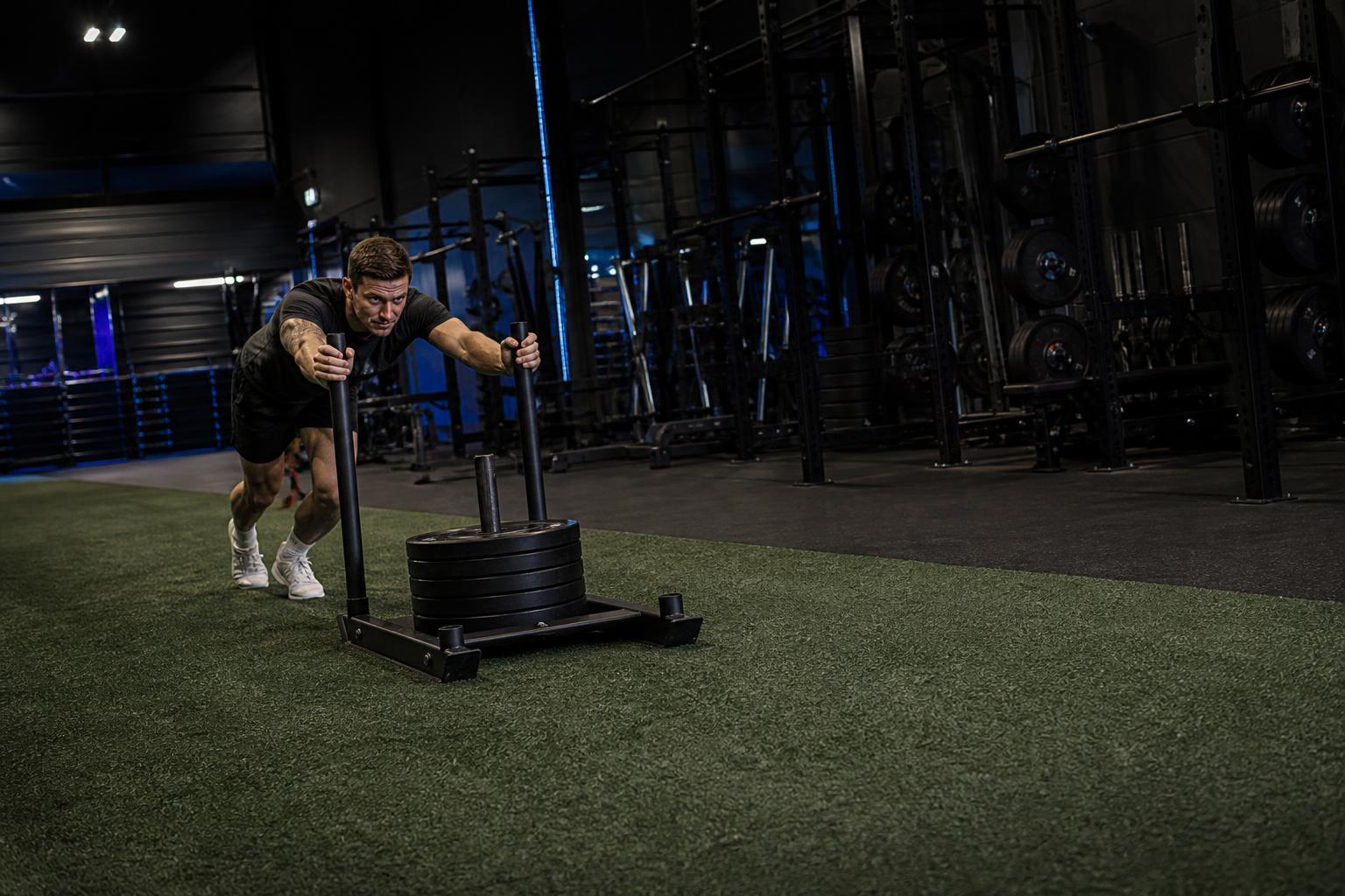 Athlete pushing a weighted sled along a green turf lane in a functional training gym